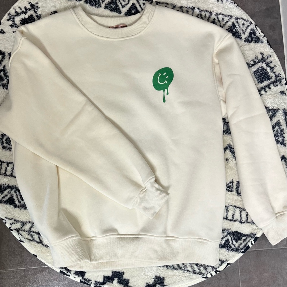 Bailey Rose cream crewneck with green smiley face.